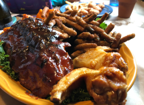 A colorful platter featuring barbecue chicken, fried items, and crispy sides on a bed of lettuce.