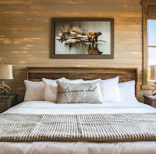 Cozy bedroom with a wooden bed, white linens, and a bear painting on the wall, creating a rustic atmosphere.