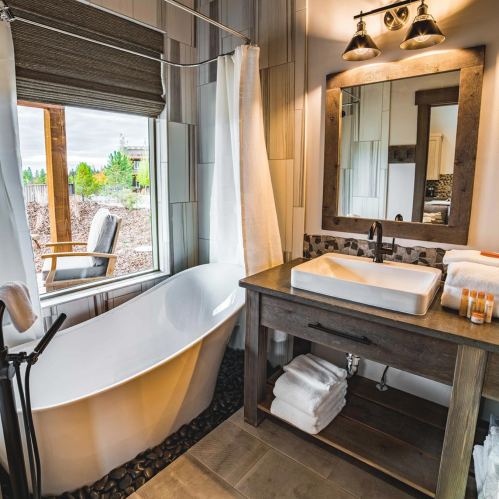 A modern bathroom featuring a freestanding tub, wooden vanity, and large window with natural light.