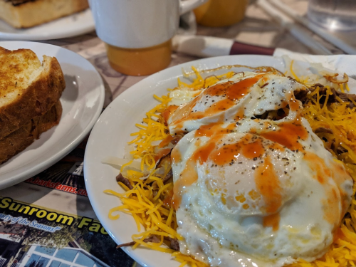 A plate of cheesy eggs topped with sauce, served alongside a slice of toasted bread.