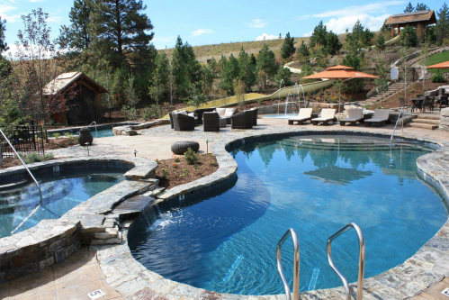 A scenic outdoor pool area with stone features, lounge chairs, and trees under a clear blue sky.
