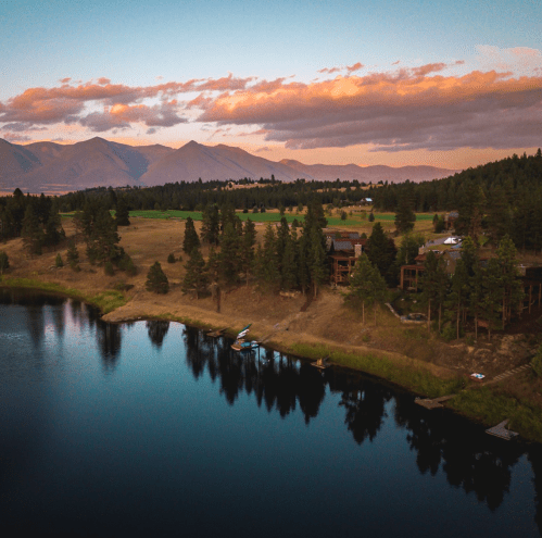 A serene lake surrounded by trees and mountains, reflecting a colorful sunset in the sky.