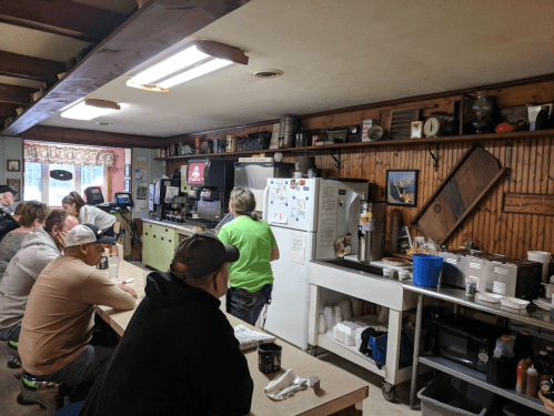 A cozy diner interior with patrons seated at a counter, while a staff member prepares food in the kitchen area.