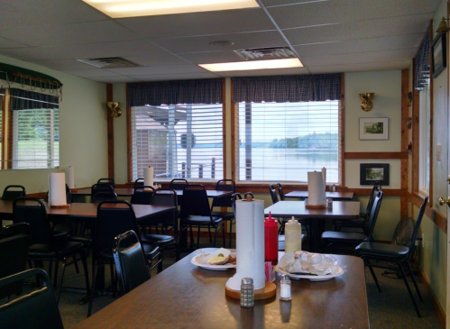 A cozy restaurant interior with empty tables, paper towels, and a view of a lake through large windows.