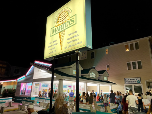 A busy ice cream shop at night, with a bright sign and a crowd of people enjoying treats outside.