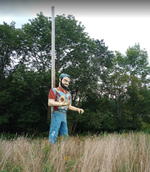 A large, colorful statue of a man in a floral shirt stands in a grassy field, surrounded by trees.