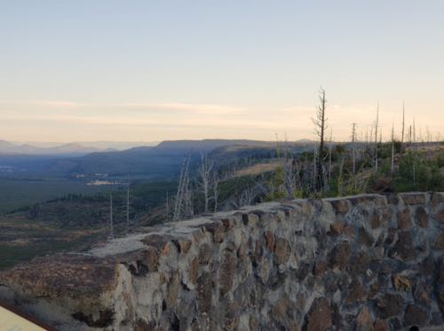 A rocky viewpoint overlooking a vast landscape with distant mountains and sparse trees under a clear sky.