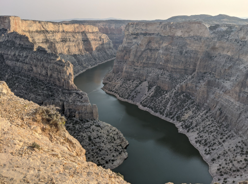 A winding river flows through steep, rocky cliffs under a clear sky, showcasing a rugged, natural landscape.