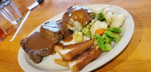 A plate of meatloaf with gravy, mashed potatoes, and mixed vegetables, served with toasted bread on the side.