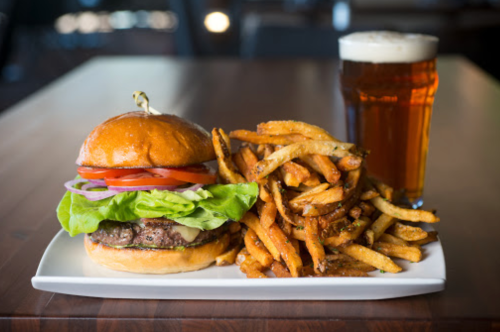 A juicy burger with lettuce, tomato, and onion, served with crispy fries and a pint of beer on a wooden table.