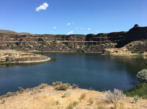 A serene lake surrounded by rocky cliffs and sparse vegetation under a clear blue sky.