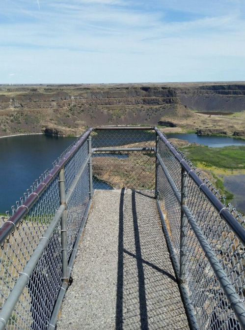 View from a fenced lookout point overlooking a river and rocky landscape under a clear blue sky.