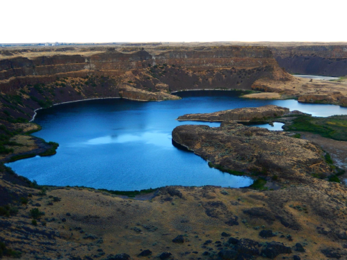 A serene blue lake surrounded by rocky cliffs and dry land under a clear sky.