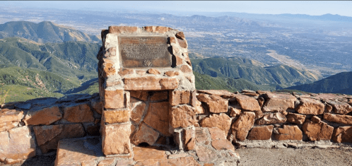A stone monument overlooks a vast mountainous landscape under a clear blue sky.