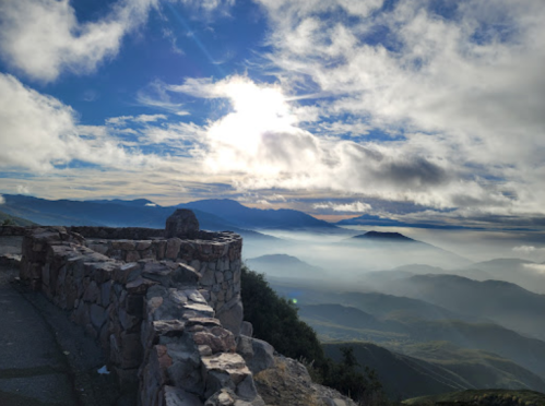A scenic view from a stone overlook, featuring mountains shrouded in mist under a cloudy sky.