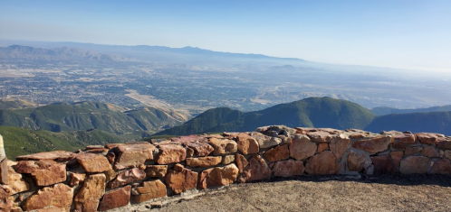 A panoramic view from a rocky overlook, showcasing mountains and a valley under a clear blue sky.