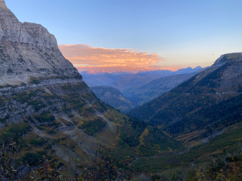 A scenic mountain landscape at sunset, featuring steep cliffs and a valley with colorful foliage.