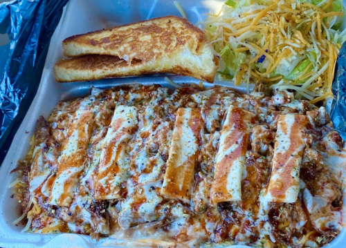 A takeout container with cheesy enchiladas, a side of salad, and two slices of toasted bread.