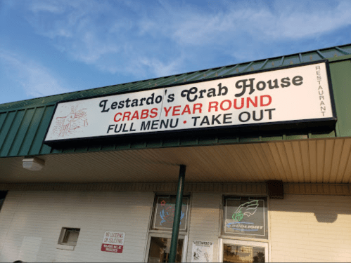 Sign for Lestardo's Crab House featuring "Crabs Year Round" and "Full Menu • Take Out" against a blue sky.