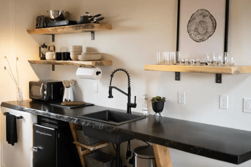 A modern kitchen with a black countertop, shelves, a sink, and various kitchen appliances and tableware.