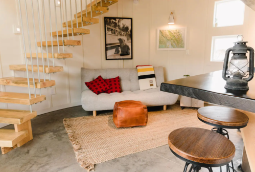 Cozy living space with a gray sofa, wooden stairs, a lantern, and a warm color palette.