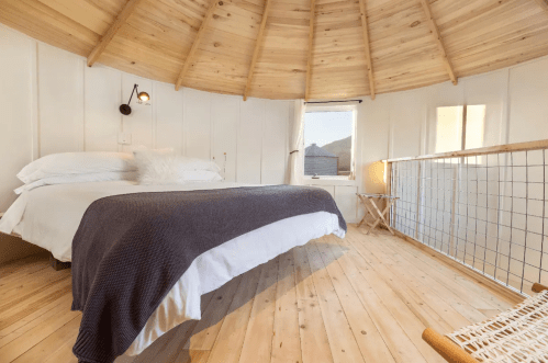 Cozy circular bedroom with wooden walls, a bed with white linens, and a warm, inviting atmosphere.