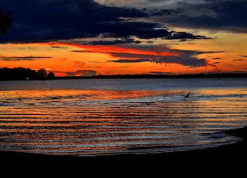A serene sunset over a calm lake, with vibrant orange and purple hues reflecting on the water's surface.
