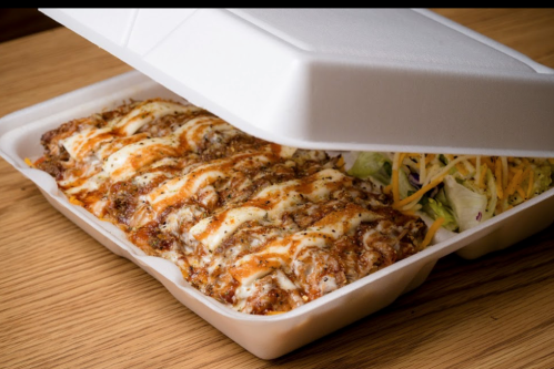 A takeout container with cheesy enchiladas and a side of salad, partially open on a wooden surface.