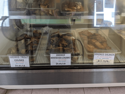 Display case with smoked fish: trout, whitefish, and salmon, each labeled with prices per pound.