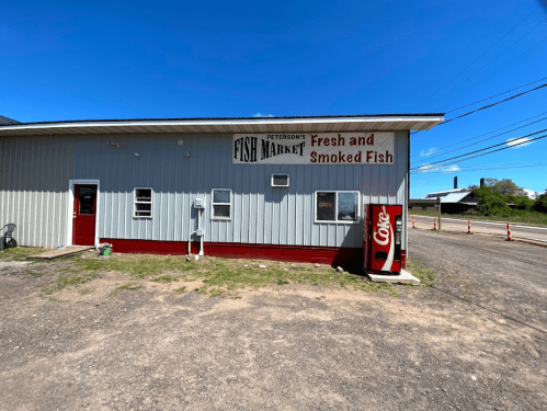 Exterior of Peterson's Fish Market, featuring a sign for fresh and smoked fish, with a Coca-Cola vending machine nearby.