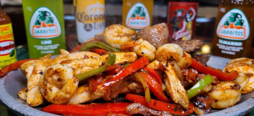 A vibrant plate of shrimp and chicken fajitas with bell peppers, surrounded by various colorful beverages.