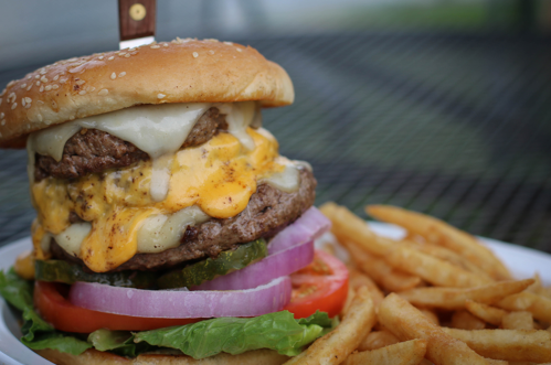 A juicy cheeseburger with layers of beef, melted cheese, lettuce, tomato, onion, and pickles, served with crispy fries.