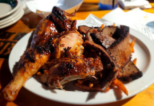 A plate of grilled chicken, ribs, and brisket served with sweet potato fries.