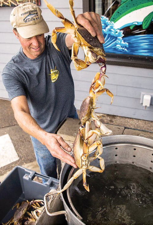 A man in a cap lifts crabs from a bucket, preparing them for sale at a seafood market.