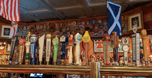 A bar with various beer taps and flags, decorated with numerous badges and memorabilia on the walls.