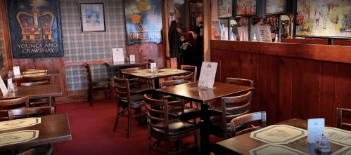 Cozy restaurant interior with wooden tables, chairs, and colorful wall art, creating a warm atmosphere.
