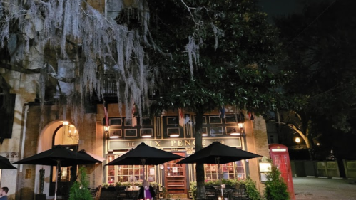 A cozy restaurant exterior at night, featuring outdoor seating and a large tree draped with Spanish moss.
