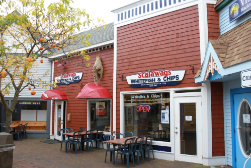Exterior of Scalawags Whitefish & Chips restaurant, featuring red awnings and outdoor seating in a quaint shopping area.