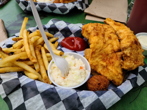 A plate of fried chicken, coleslaw, fries, and a cornbread muffin, served with ketchup on a checkered paper.