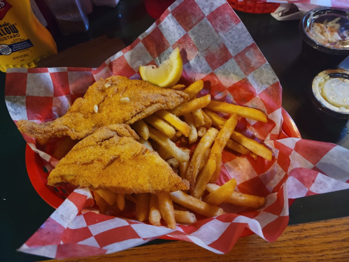 A basket of golden fried fish fillets with a lemon wedge, served with crispy French fries and dipping sauces.
