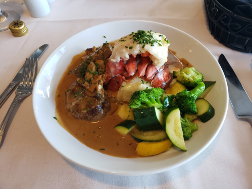 A plate of lobster, mashed potatoes, and mixed vegetables in a savory sauce, garnished with herbs.