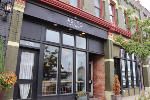 Exterior of Astro Coffee shop featuring large windows, a black sign, and colorful brick walls.