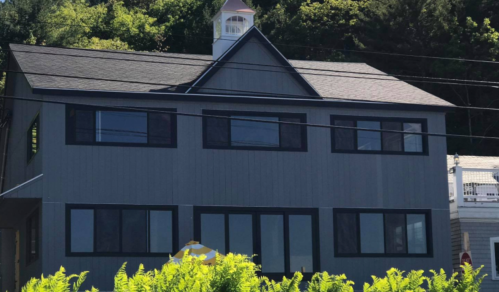 A modern gray house with large windows and a cupola on the roof, surrounded by greenery.