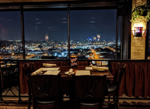 A cozy restaurant table with a view of a city skyline at night, illuminated by city lights.