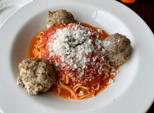 A plate of spaghetti topped with marinara sauce, grated cheese, and three meatballs.