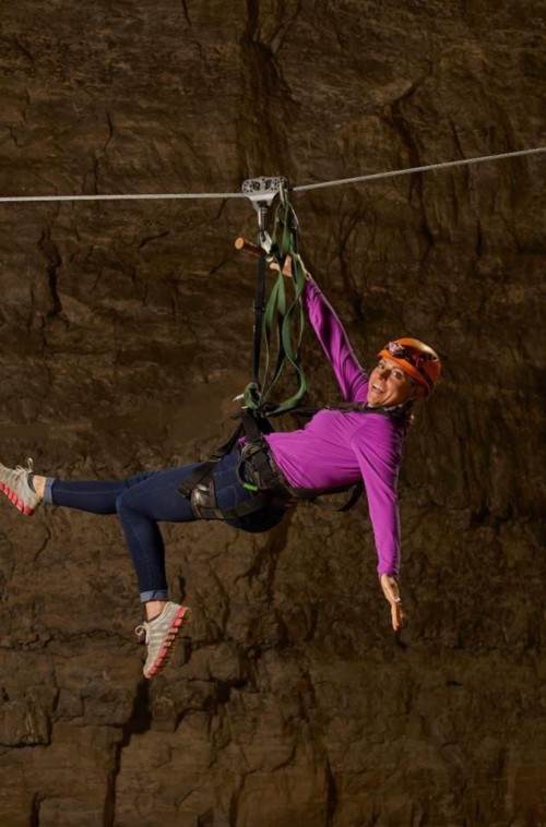 A person in a helmet and harness zip-lining through a cave, smiling and enjoying the adventure.