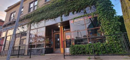 A storefront with large windows covered in ivy, featuring a sign for takeout and the name "Melting Point."