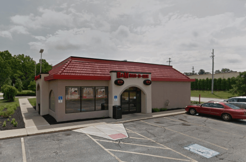 A fast-food restaurant with a red roof and signage, surrounded by parking spaces and greenery.