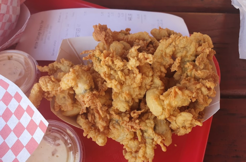 A serving of crispy fried seafood in a paper tray, accompanied by dipping sauces on a red tray.