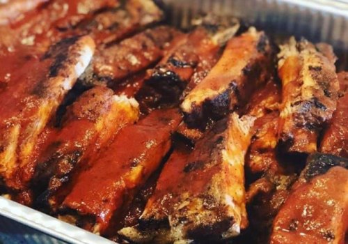 A close-up of a tray filled with glazed, barbecued ribs, showcasing a rich, smoky appearance.
